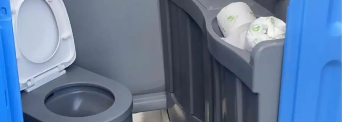 Interior of a deluxe porta potty with a flushing toilet and a built-in sink with foot pump