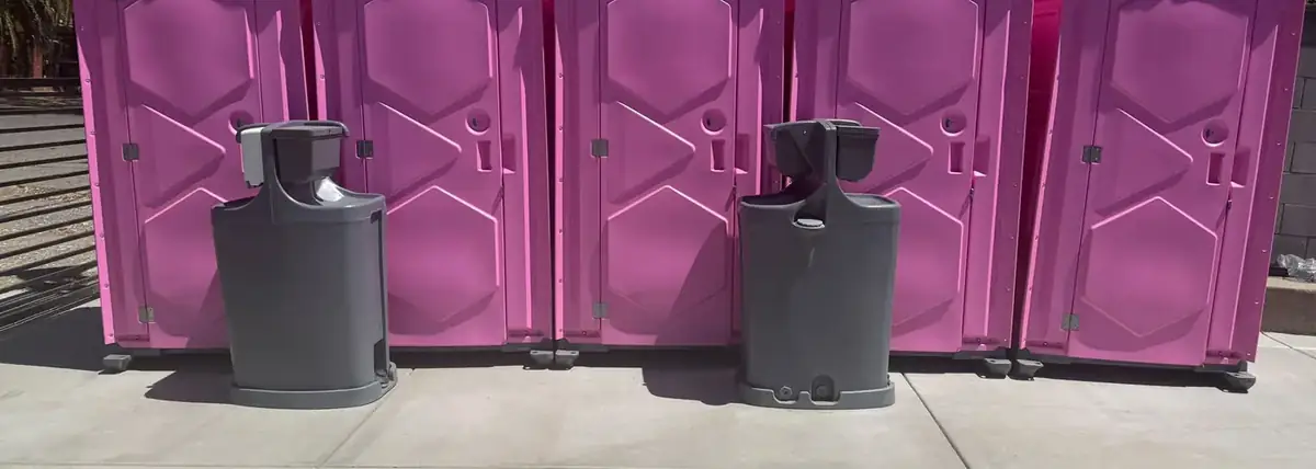 Row of pink portable restrooms with two hand washing stations in front