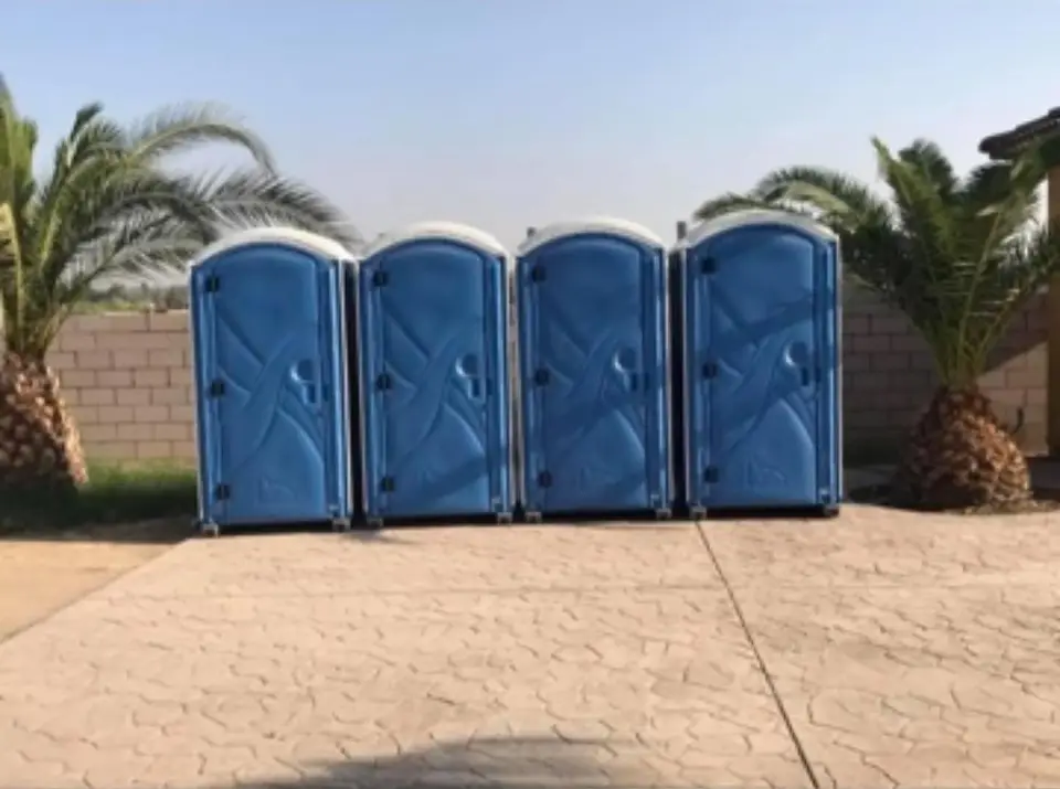 Four blue porta potties with palm trees behind