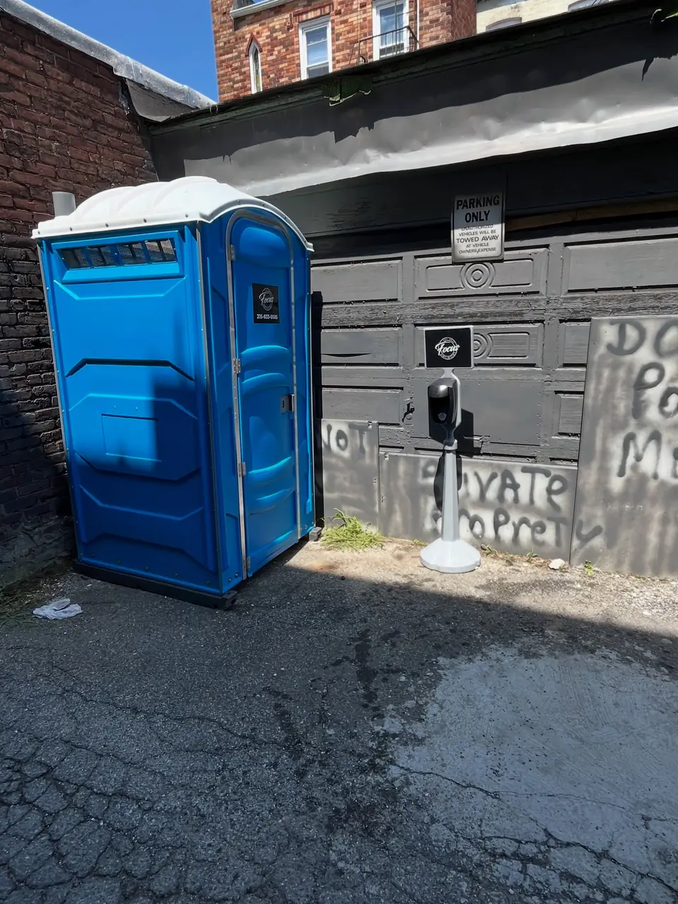 Blue porta potty with a hand washing station in a narrow alley next to a building