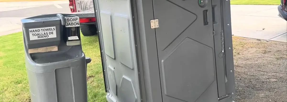 Grey porta potty and hand washing station on a lawn