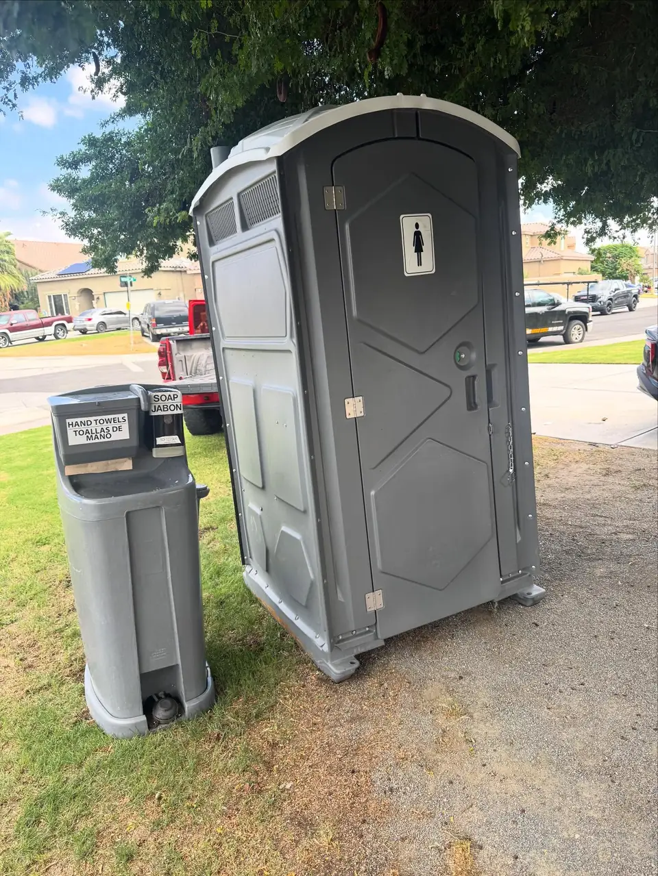 Grey porta potty and hand washing station on a front lawn
