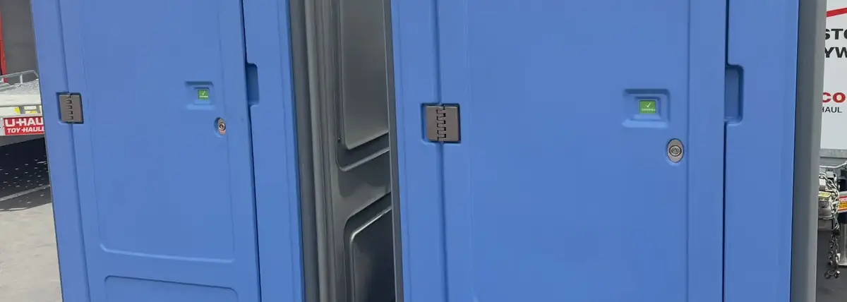 Two blue standard porta potties side by side on a paved lot
