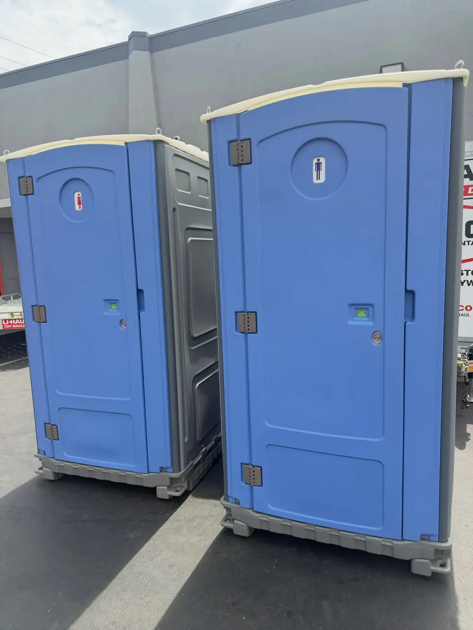 Two blue standard porta potties on a paved lot